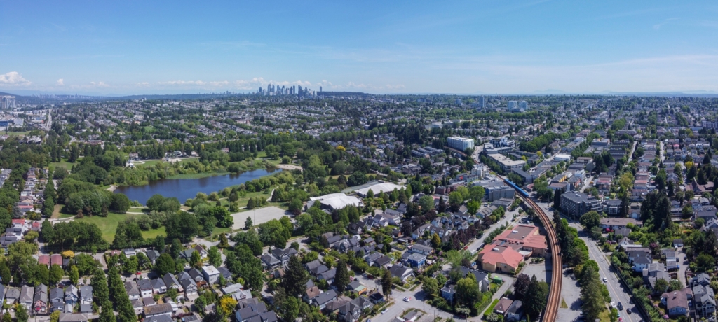 Aerial view over Trout Lake in John Hendry Park with blocks of detached houses, the elevated SkyTrain guideway and the downtown Vancouver skyline behind, Kensington-Cedar Cottage, Vancouver