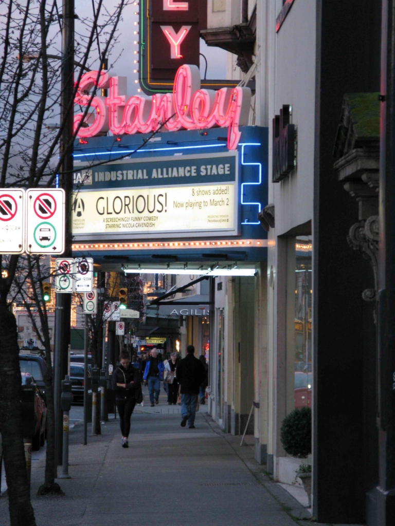 The neon Stanley Theatre marquee and storefronts along the sidewalk on Granville Street at 12th Avenue in South Granville, Vancouver